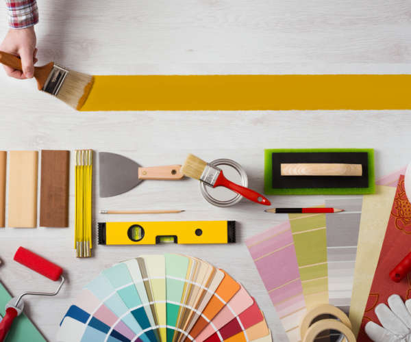 Decorator holding a paint brush and painting a wooden surface, work tools and swatches at bottom, banner with copy space